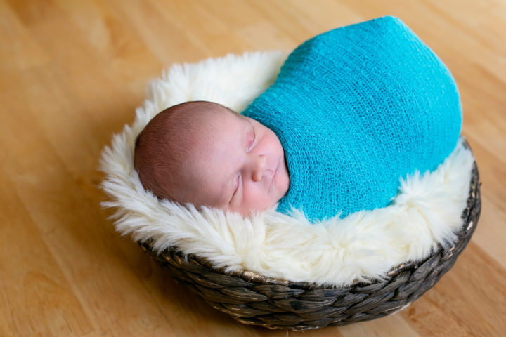 A new baby wrapped in a turquoise wrap in a wicker basket