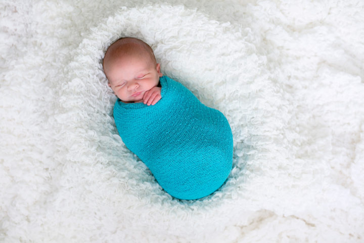 A new baby swaddled in a turquoise wrap on a textured white blanket