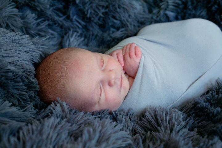 A new baby swaddled in a grey wrap on a fluffy grey blanket